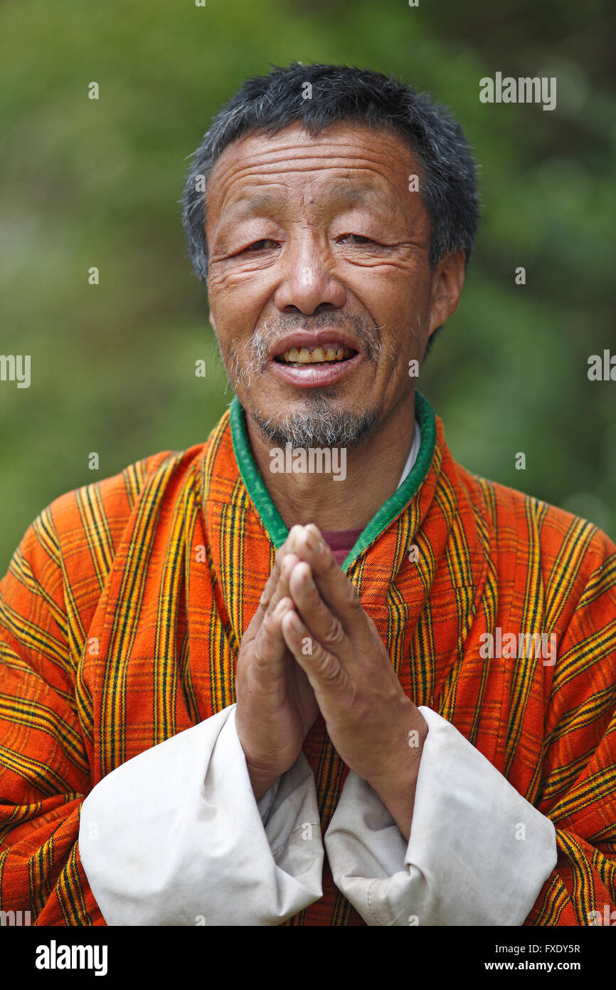L'uomo, 58 anni, in Gho-vestito con le mani incrociate, ritratto, Jakar, Bumthang Valley, Bhutan Foto Stock