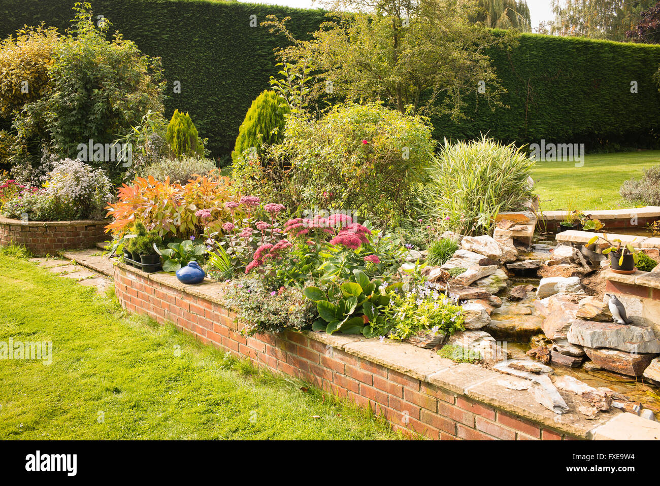Mista confine erbaceo con mattoni poco profonda parete di ritegno e una piccola fontana in un giardino inglese Foto Stock