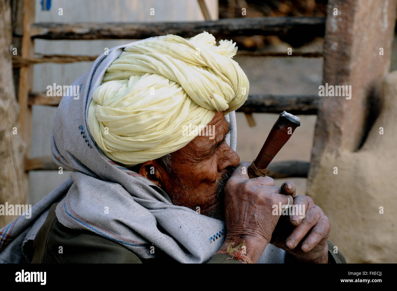 Un vecchio uomo fuma la sua mattina presto tubazione di oppio e guarda su mentre la moglie prepara la sua colazione chapatis. Foto Stock