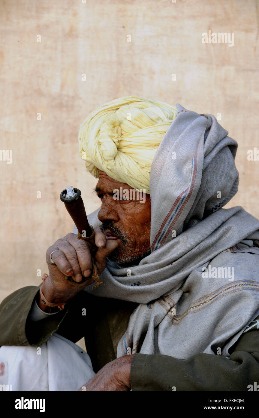 Un vecchio uomo fuma la sua mattina presto tubazione di oppio e guarda su mentre la moglie prepara la sua colazione chapatis. Foto Stock