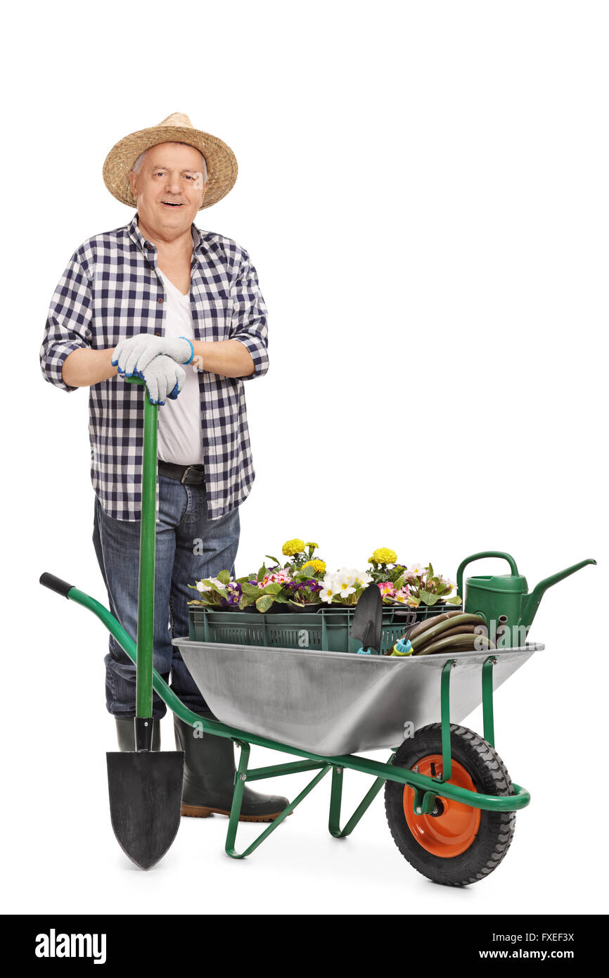A piena lunghezza Ritratto di un giardiniere matura in posa dietro una carriola piena di fiori e attrezzature da giardinaggio Foto Stock