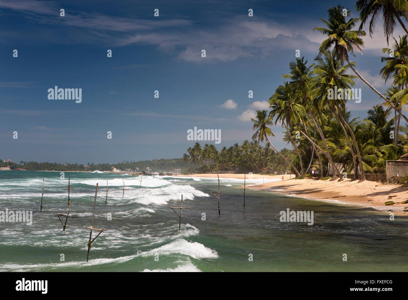 Sri Lanka, Unawatuna, Dalawella Beach, onde si infrangono in oltre di pescatori di palafitte Foto Stock