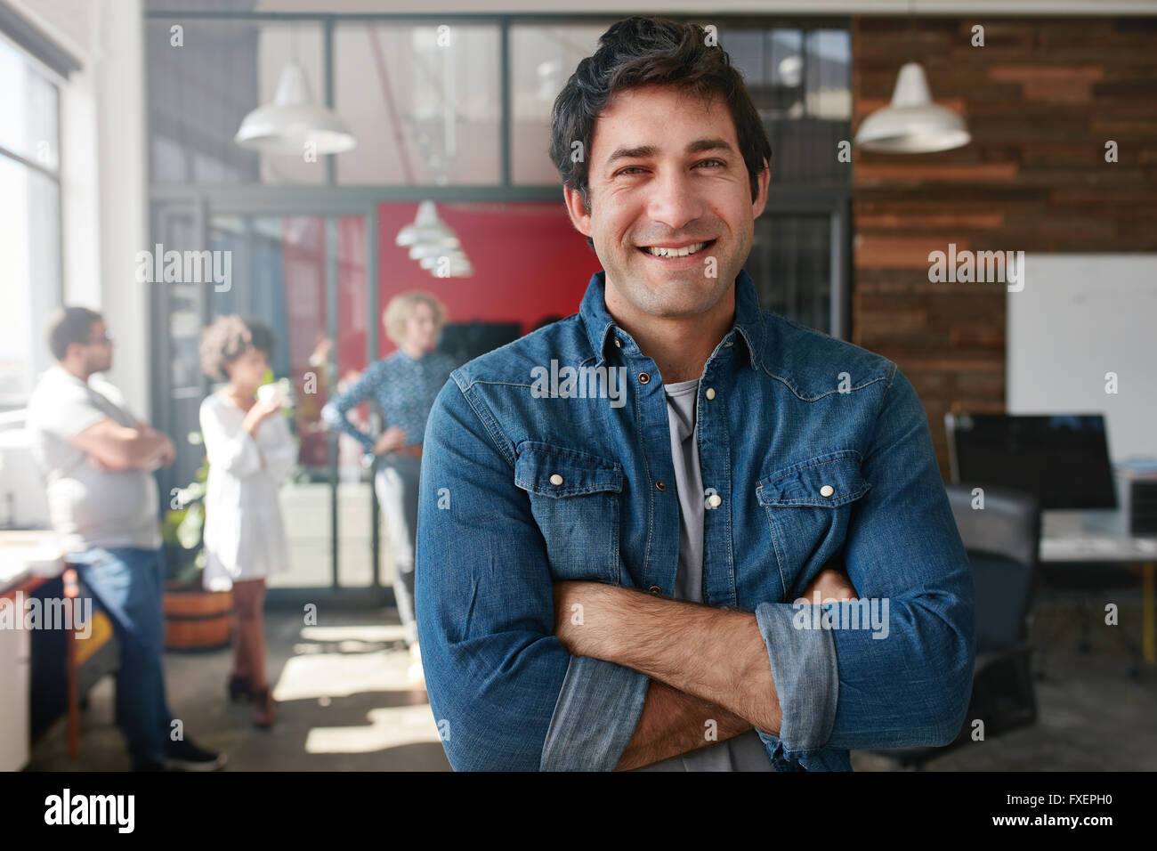 Ritratto di bel giovane uomo in piedi con le braccia incrociate a creative office. Fiducioso giovane maschio creative professional loo Foto Stock