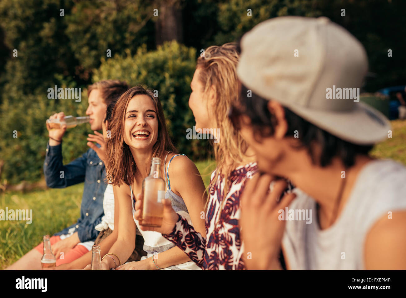 Ritratto di felice giovani seduta da un lago con birre. Gruppo di amici appendere fuori a lago. Foto Stock