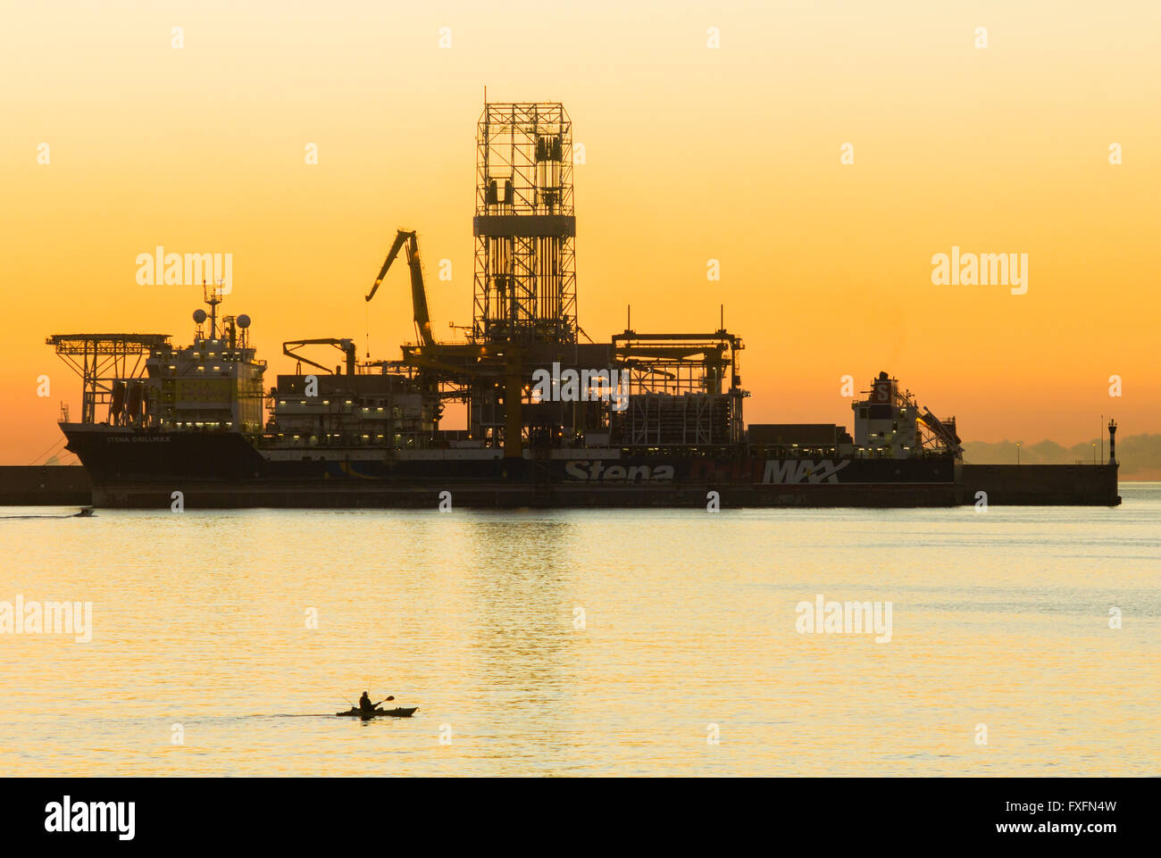 Las Palmas de Gran Canaria, Isole Canarie, Spagna, 15 aprile 2016. Meteo: un canoeist righe passato una piattaforma di perforazione a sunrise in Las Palmas porta su una gloriosa giovedì mattina a Las Palmas, la capitale di Gran Canaria. Nella foto: Las Palmas la porta è utilizzata da un certo numero di compagnie petrolifere per le riparazioni, rifornimento, e nel caso di alcune delle attrezzature veliche/piattaforme in queste immagini, per impianti di trivellazione di messa fuori servizio per lunghi periodi di tempo a causa della caduta dei prezzi del petrolio e sulla fornitura di petrolio greggio. Credito: Alan Dawson News/Alamy Live News Foto Stock