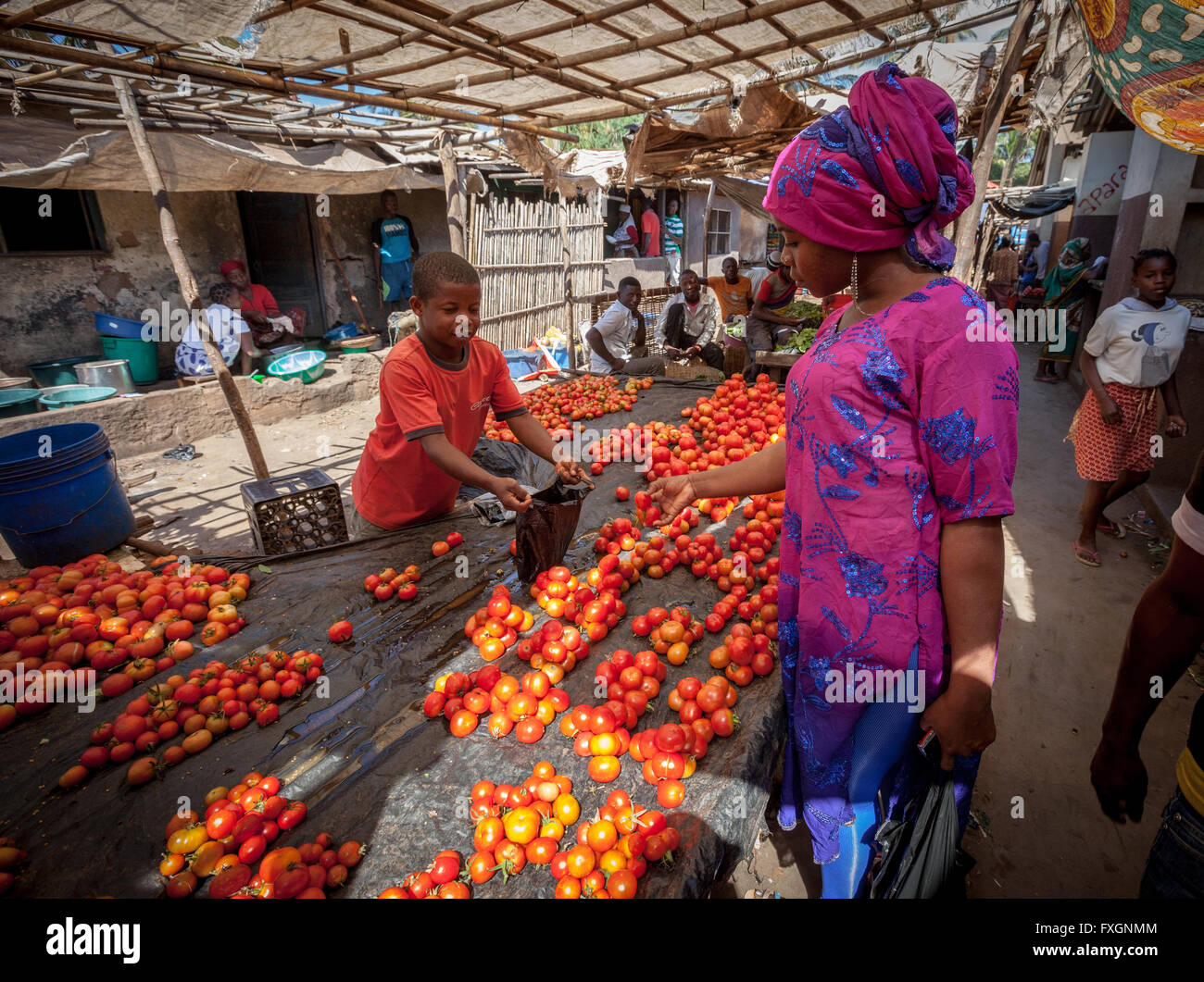 In Mozambico, un ragazzo è la vendita di pomodori al mercato di una donna con abiti colorati e velo. Foto Stock