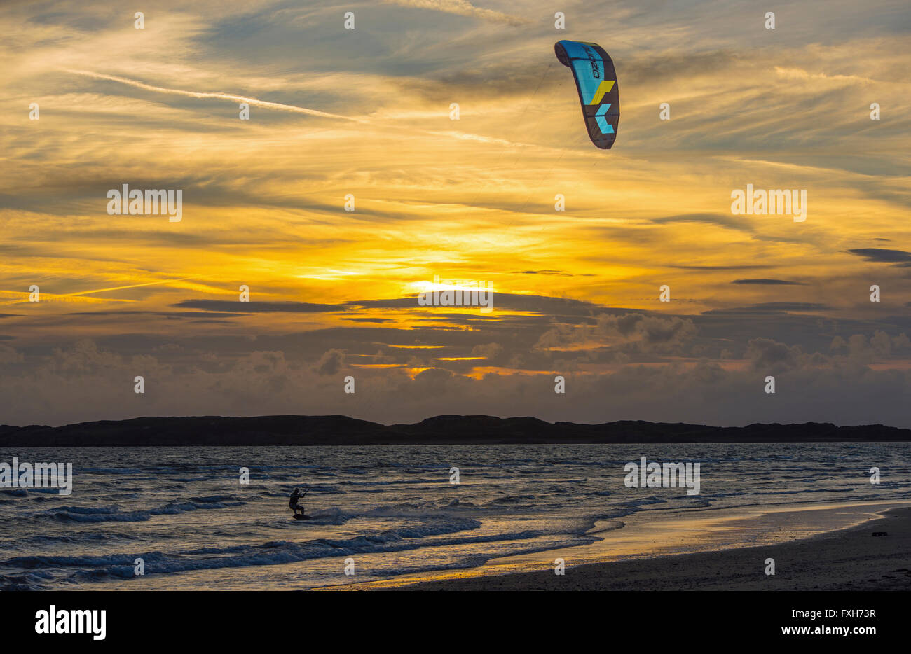 Kite Surfer il Newborough Warren sulla spiaggia di Anglesey, Galles del Nord su una serata con un bel tramonto Foto Stock