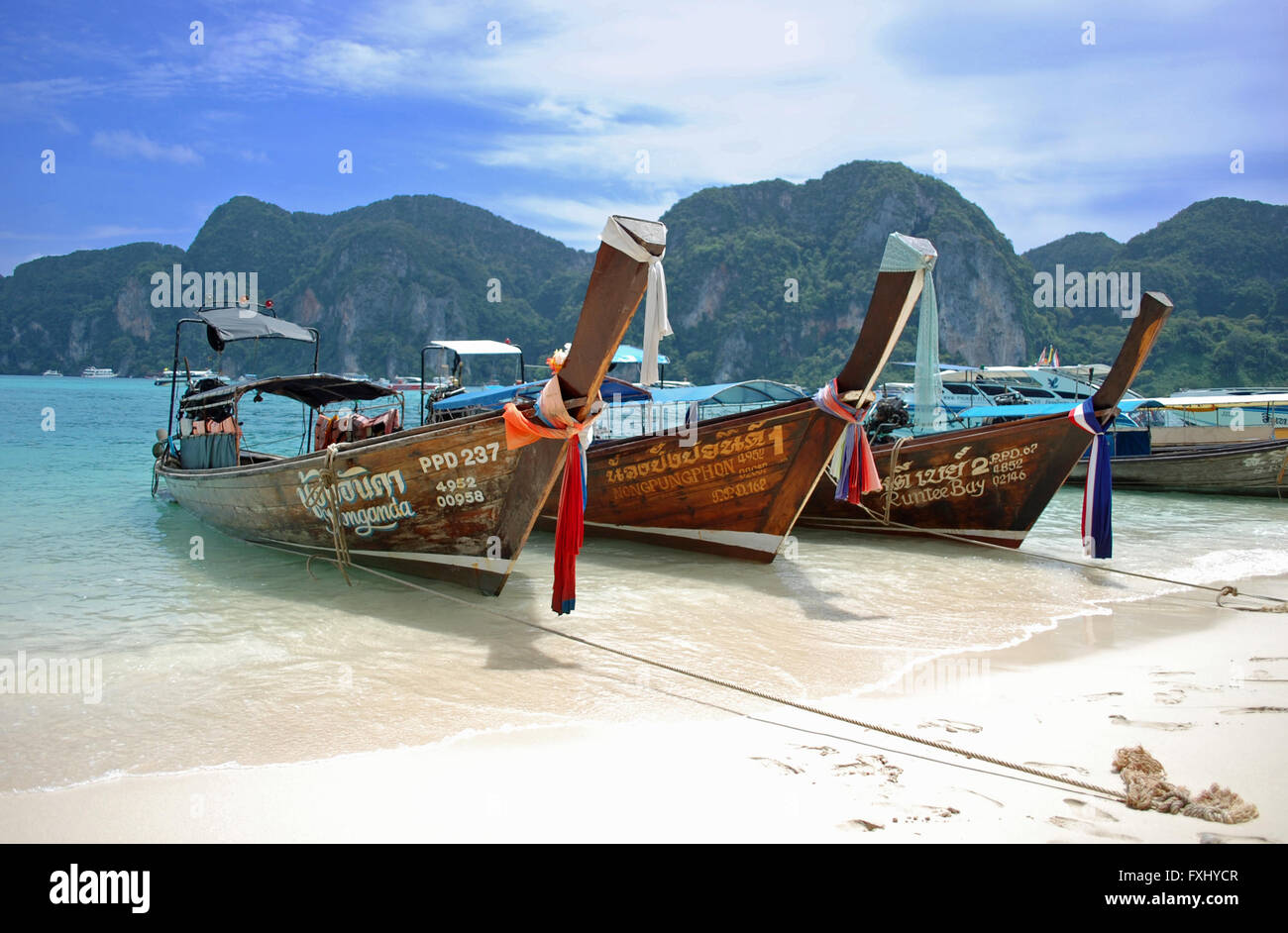 Long Tail barche, legata alla spiaggia, come le splendide acque cristalline lambiscono la riva in questa isola thailandese parardise Foto Stock
