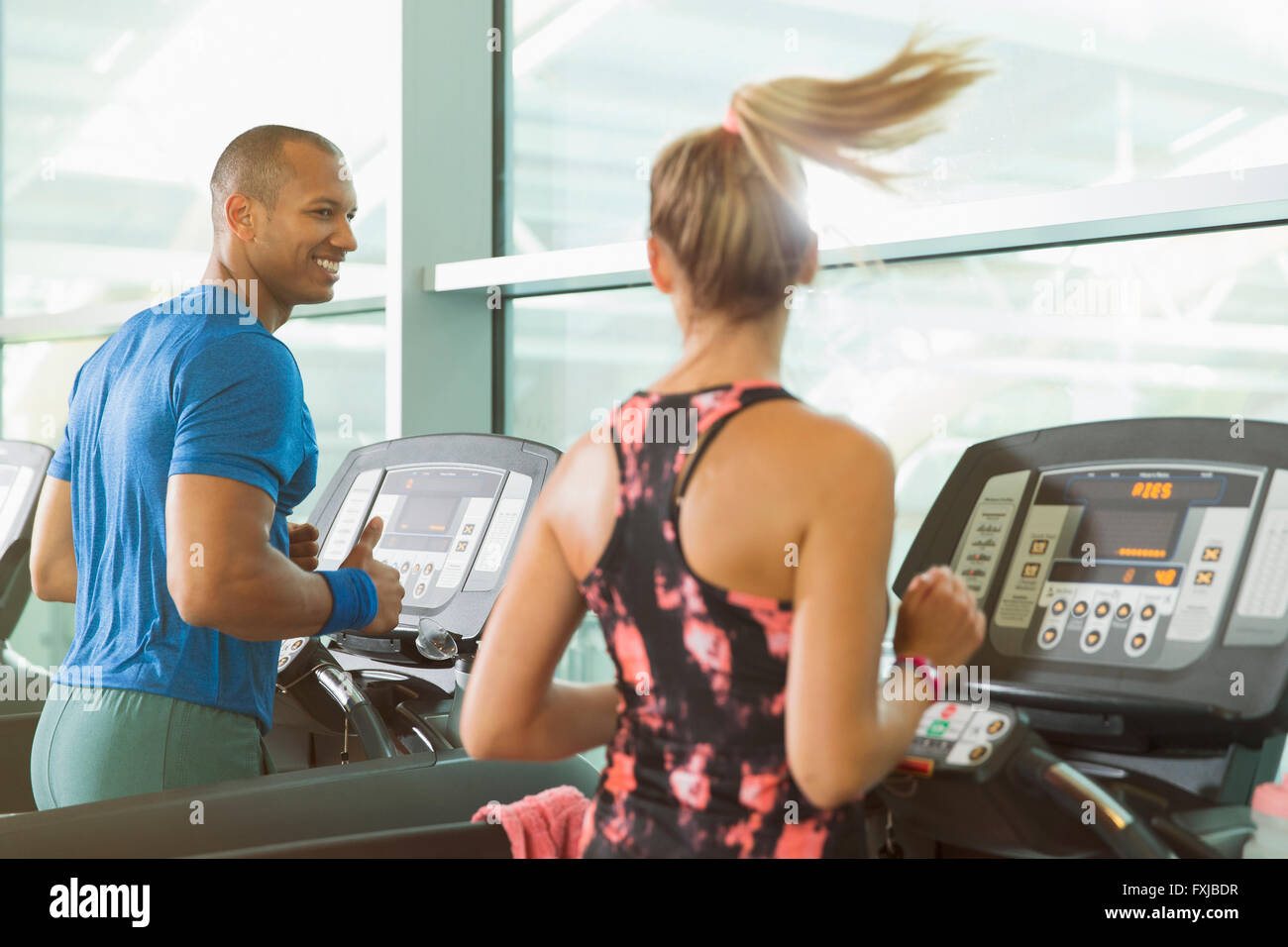 Uomo e donna che parlano e in esecuzione sul tapis roulant in palestra Foto Stock
