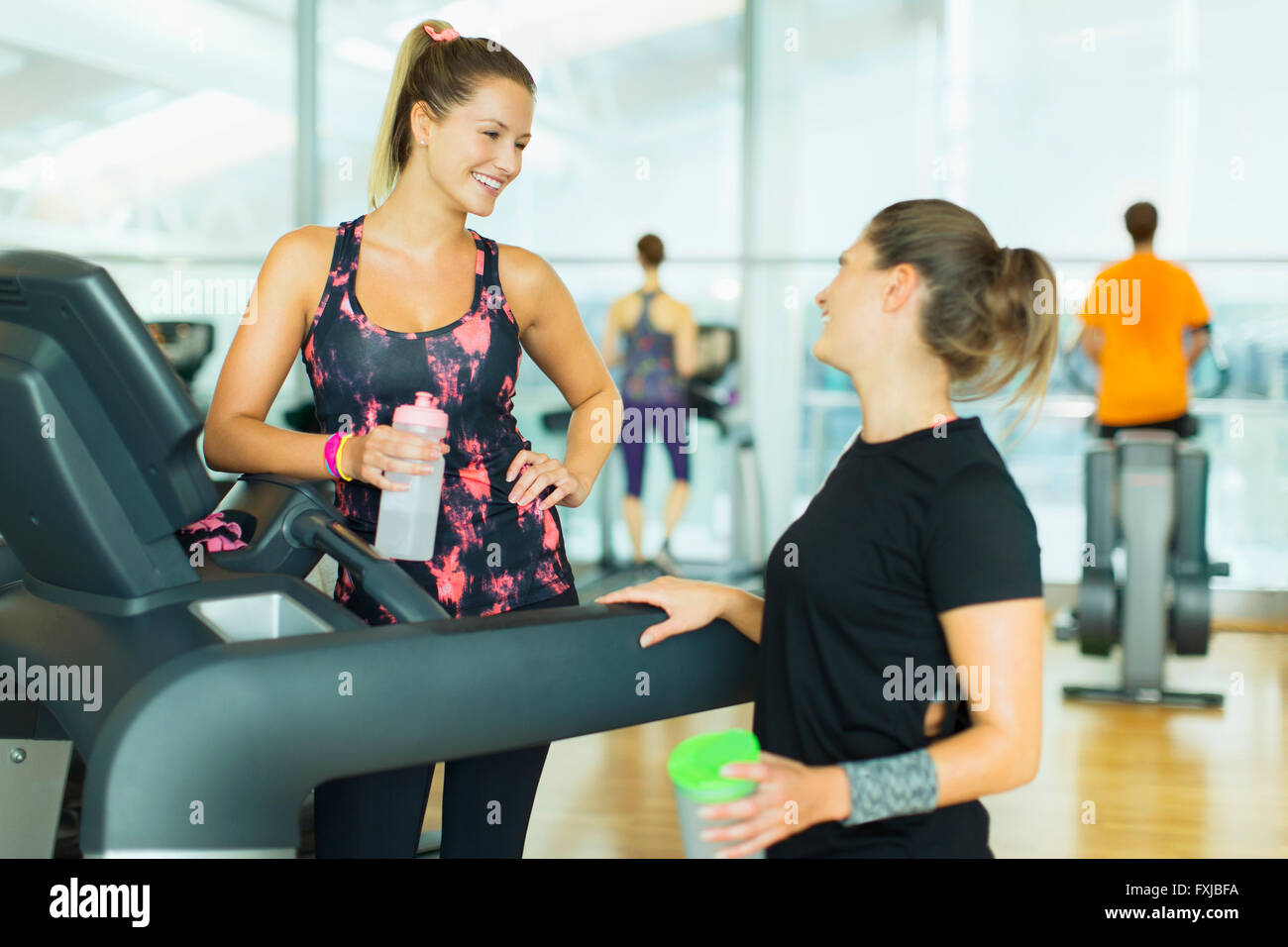 Donna sorridente in appoggio e parlare al tapis roulant in palestra Foto Stock