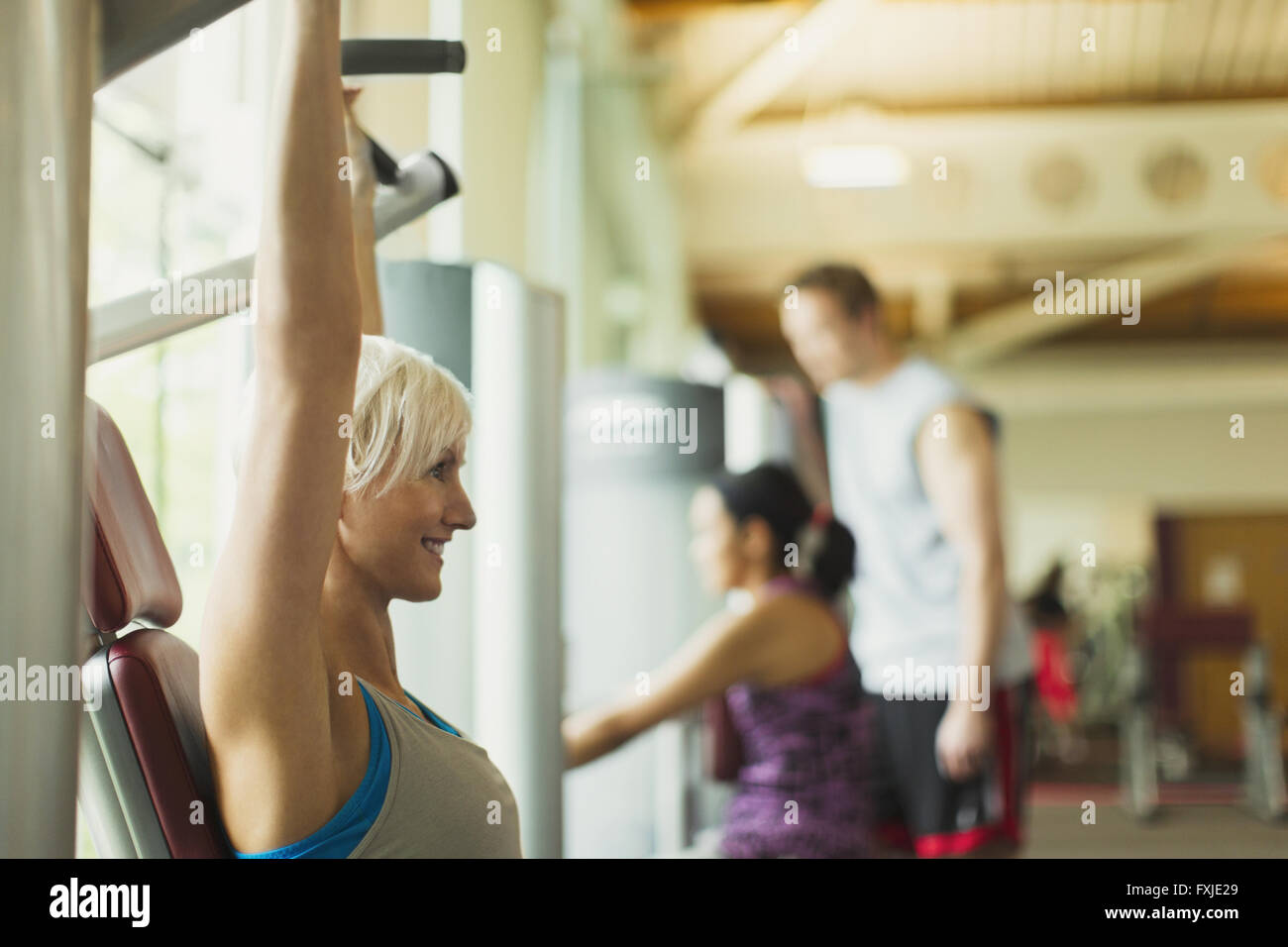 Donna sorridente con le braccia sollevate utilizzando attrezzature per esercizi in palestra Foto Stock