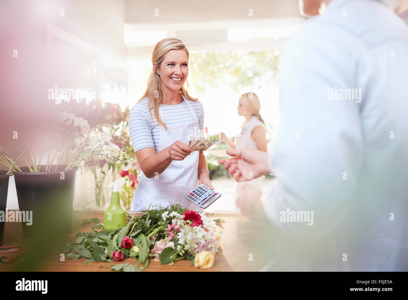 Fiorista sorridente dando il cliente cambia nel negozio di fiori Foto Stock