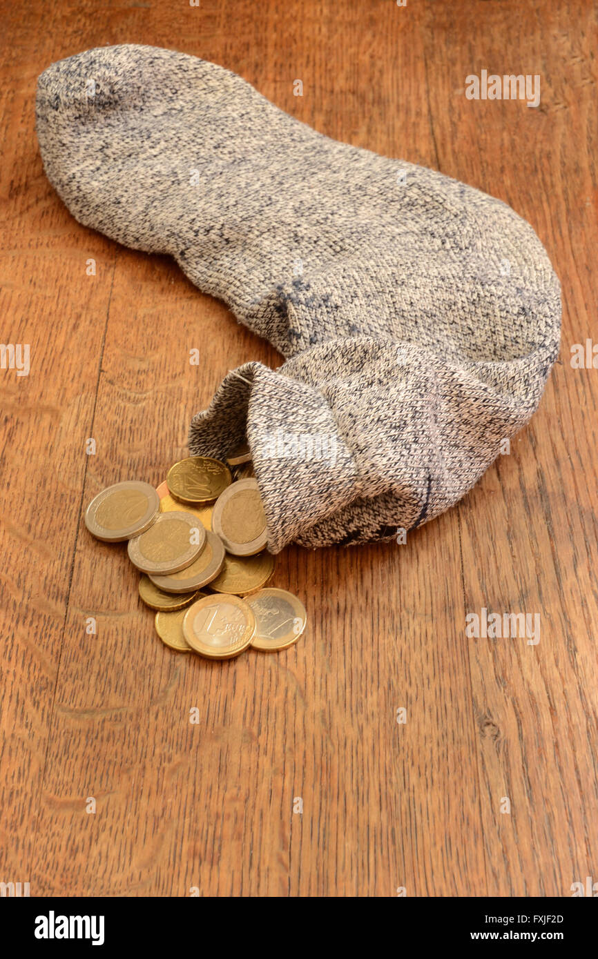 "A calza il proprio denaro' - Termine gergale americano significato per salvare. Soldi-riempito il calzino posa su pavimento in legno scuro. Le monete sono di euro. Foto Stock