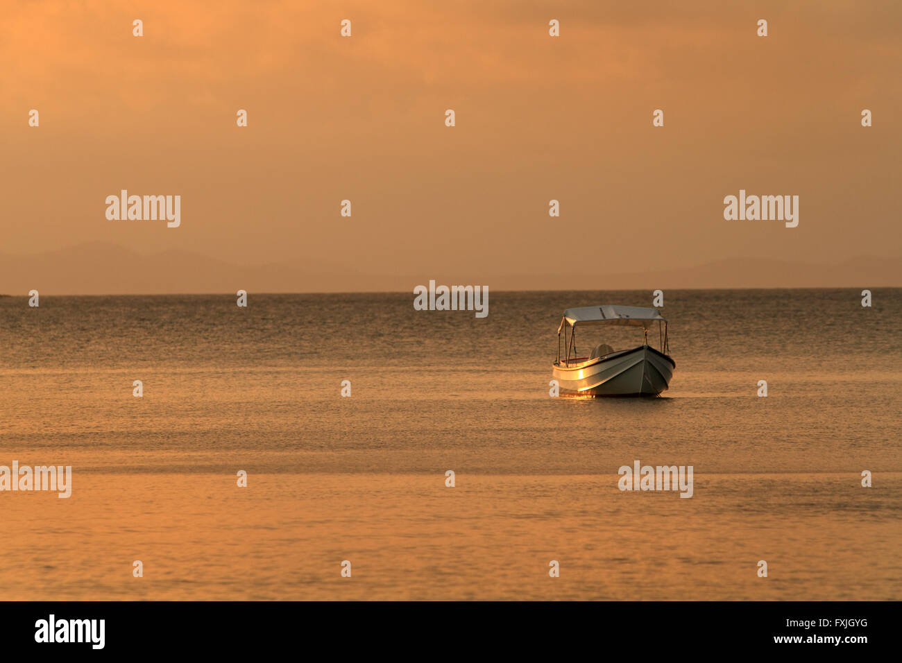 Una barca ormeggiata in acque calme al tramonto Foto Stock