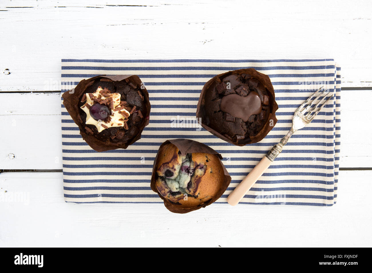 Tre deliziosi muffin al cioccolato su un blu e bianco spogliato igienico con una forcella su un bianco tavolo rustico Foto Stock