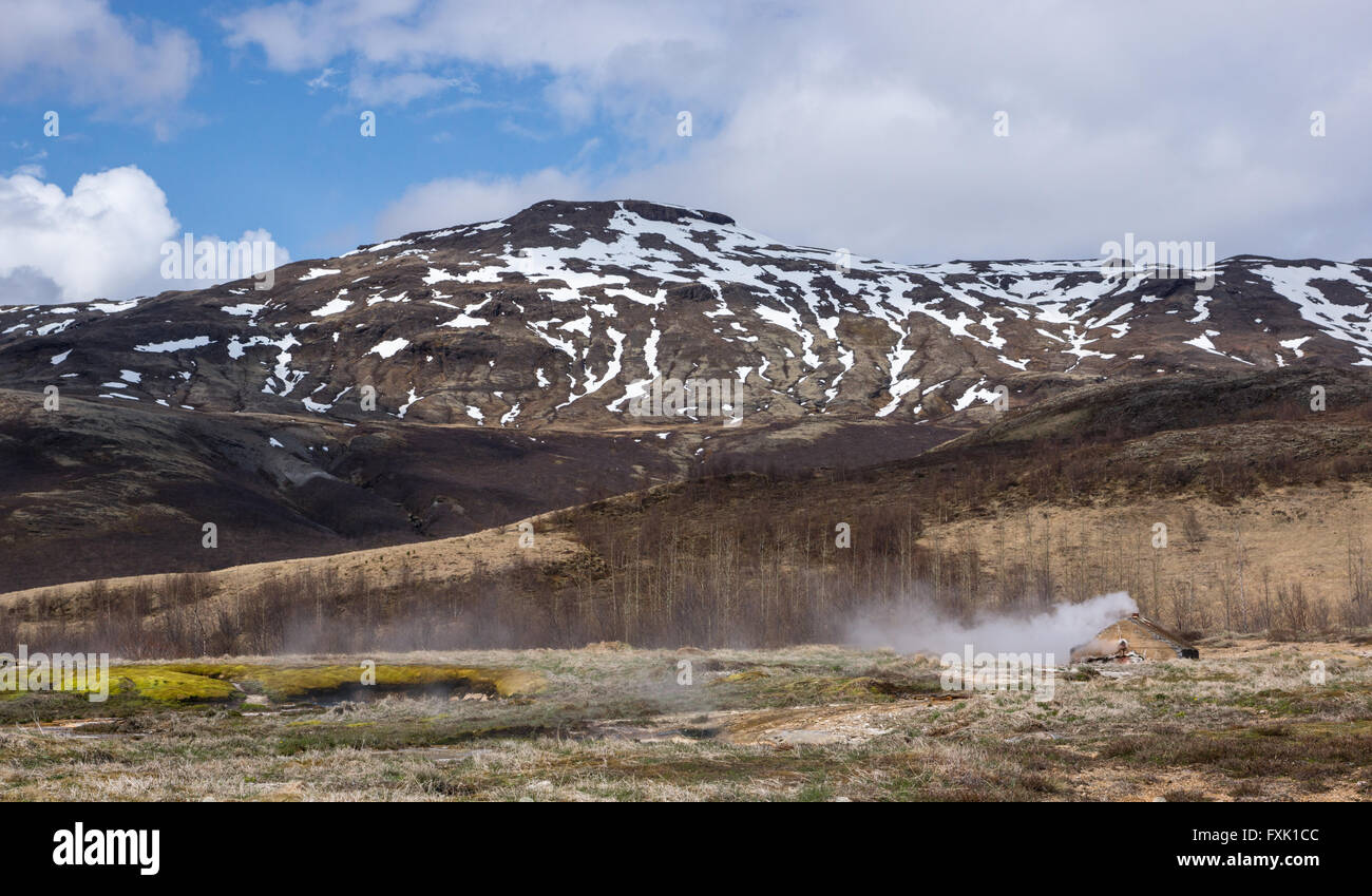 Valvola di sfiato del vapore vicino geyser nel sud dell'Islanda con montagne innevate sullo sfondo Foto Stock