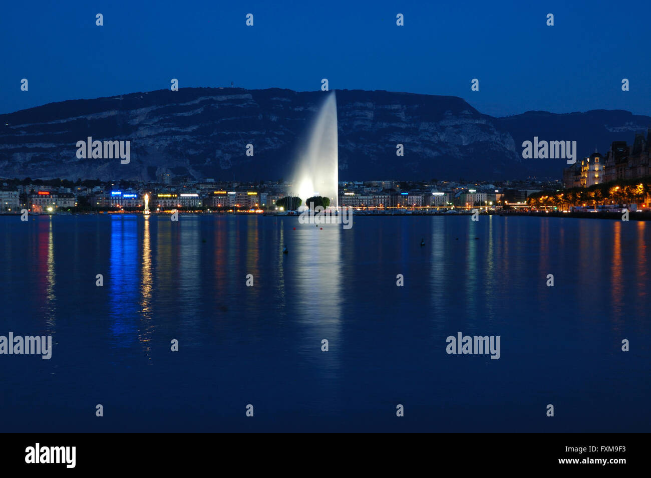 Il lago di Ginevra davanti con le luci della città e il Jet d'Eau nel centro. Foto Stock