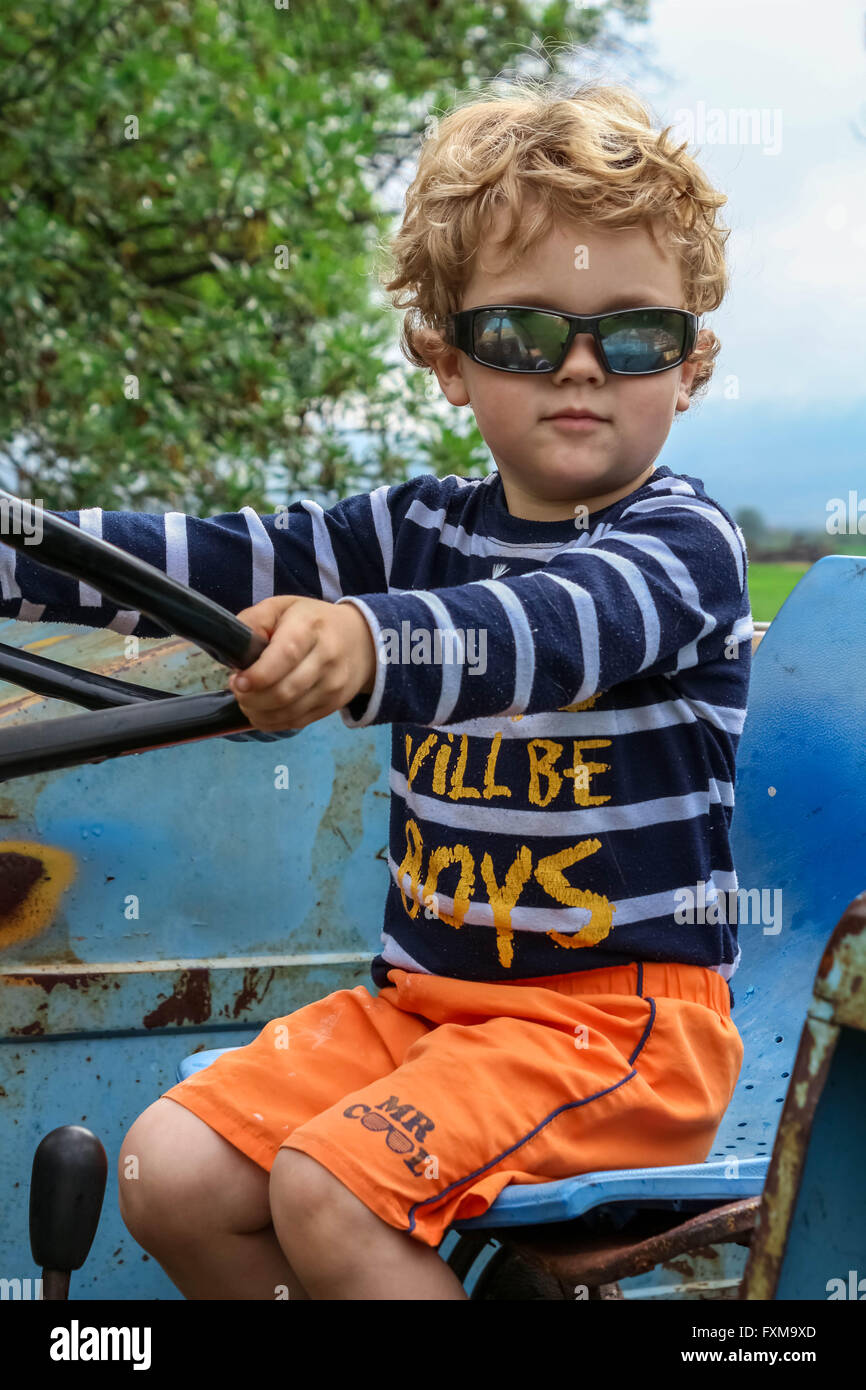 Foto del giovane ragazzo con gli occhiali da sole sul vecchio trattore blu Foto Stock