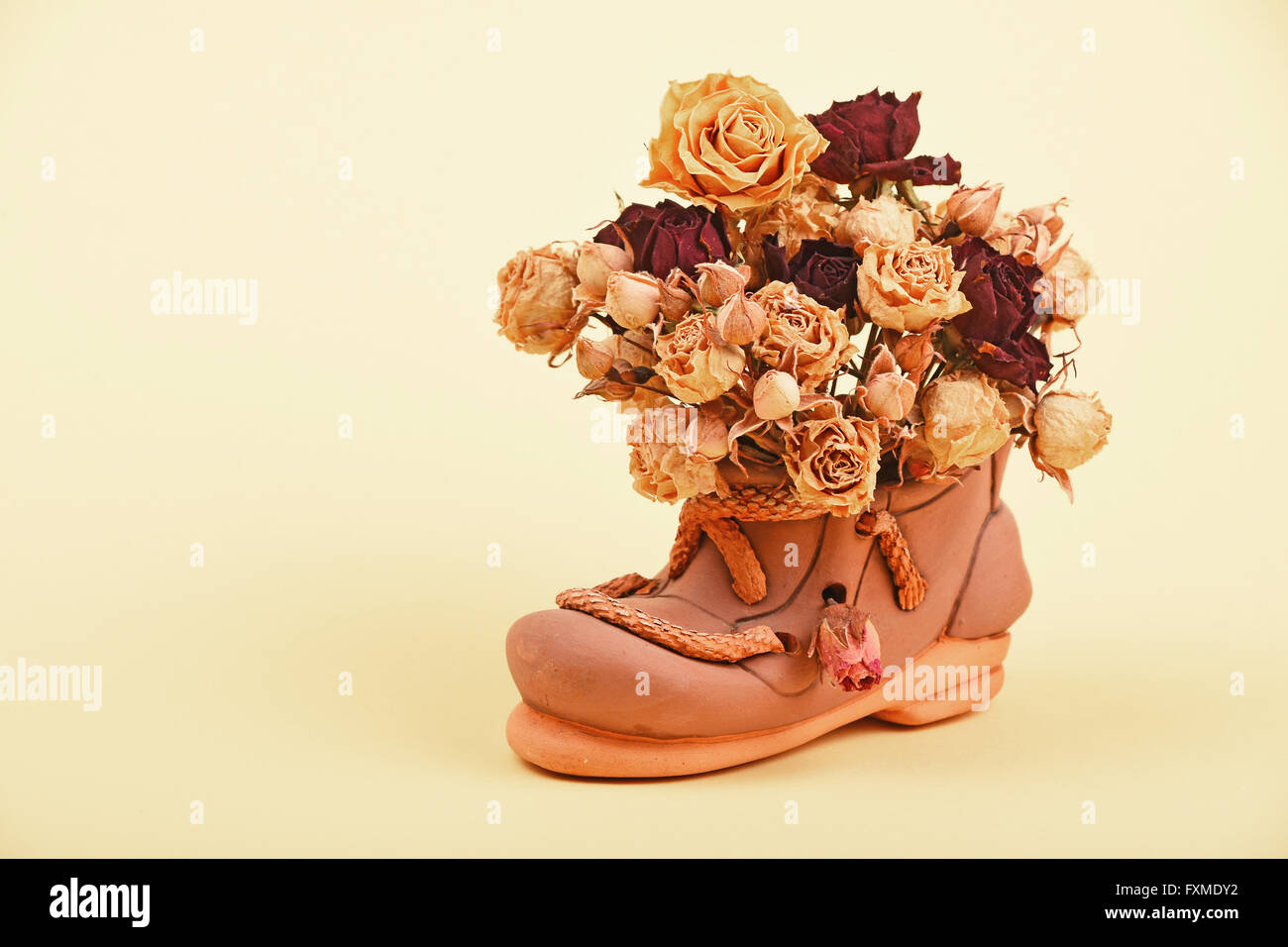 Essiccato di rosso e di giallo rose bouquet di fiori in ceramica piccolo scarpa sulla gara giallo sullo sfondo della carta Foto Stock