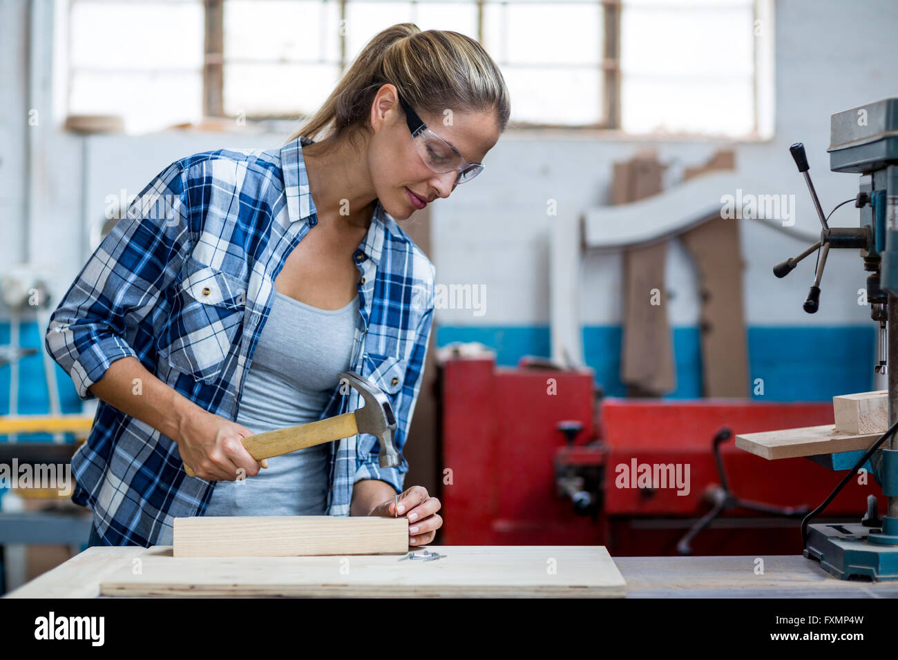 Falegname femmina tenendo un martello per guidare chiodo in un asse di legno Foto Stock