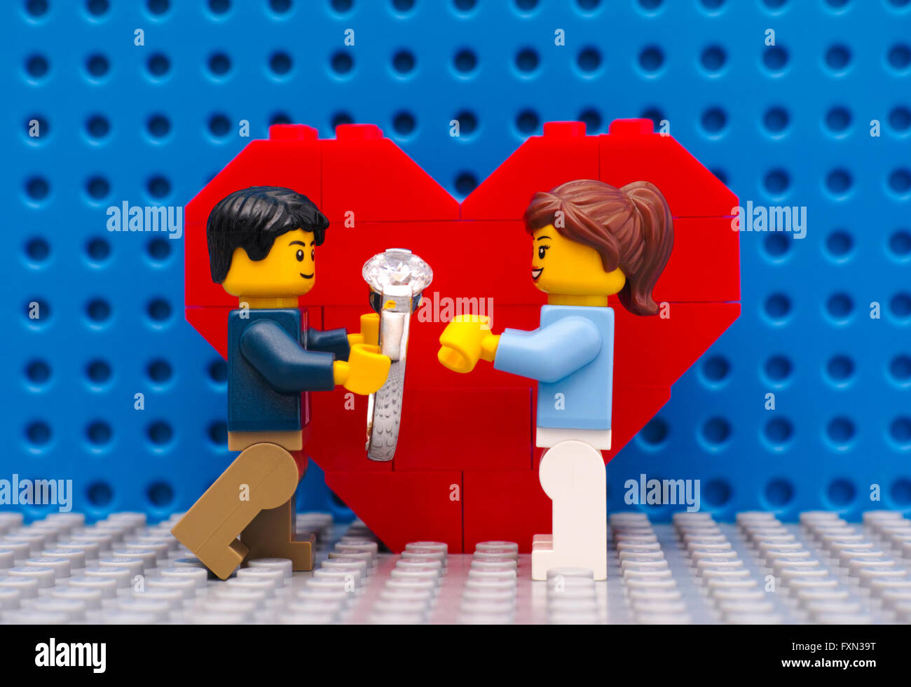 Lego uomo con anello rende la proposta di matrimonio alla sua ragazza in piedi nella parte anteriore del cuore su Lego grigio a piastra di base. Foto Stock