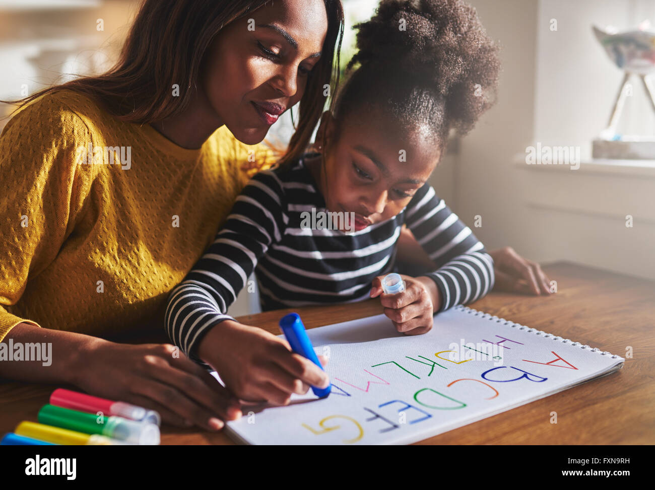 Bambina iscritto l'alfabeto con la madre a casa Foto Stock