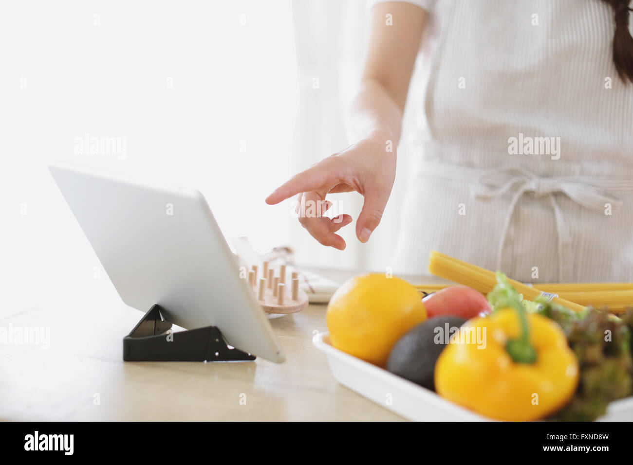 Attraente giovane donna giapponese cottura a casa con la compressa Foto Stock