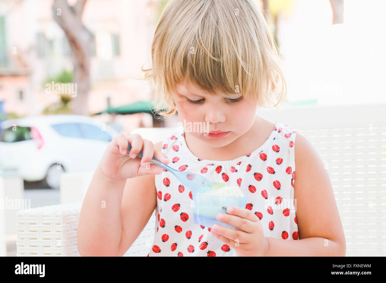 Carino biondo Caucasian Baby girl mangia frozen yogurt con gelato, chiudere fino all'aperto verticale con naturale alta luce chiave Foto Stock