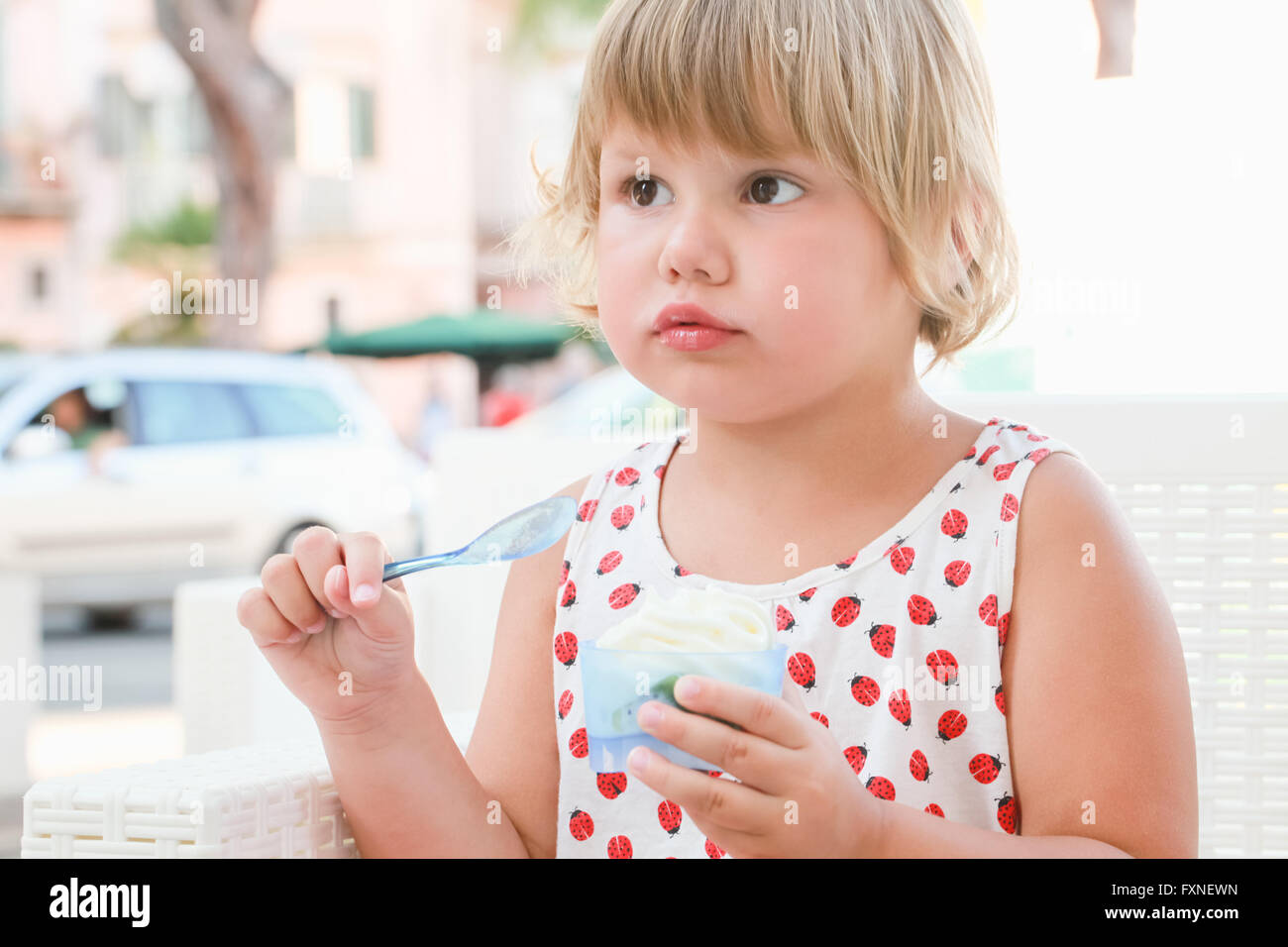 Carino biondo Caucasian Baby girl mangia lo yogurt con gelato e frutta, chiudere fino all'aperto verticale con naturale alta luce chiave Foto Stock