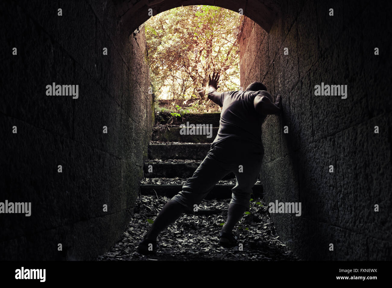 Giovane uomo stanco lascia la pietra scura tunnel con estremità incandescente Foto Stock
