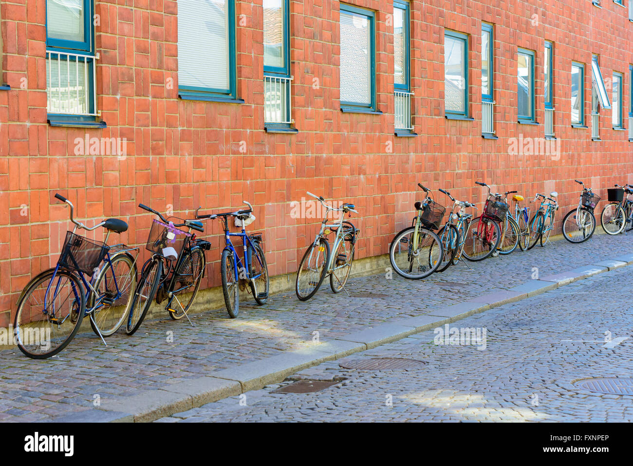 Lund, Svezia - 11 Aprile 2016: Biciclette parket in una riga al di fuori di un edificio di mattoni rossi. Street è costituito di blocchi di pietra. Foto Stock
