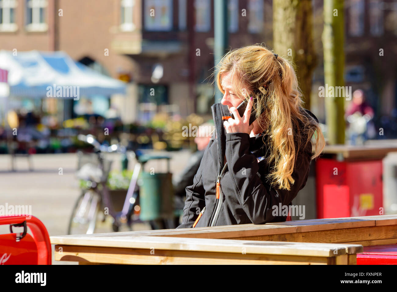 Lund, Svezia - 11 Aprile 2016: donna bionda in capelli lunghi parlando nel suo telefono cellulare mentre appoggiato su di una ringhiera di legno. Foto Stock