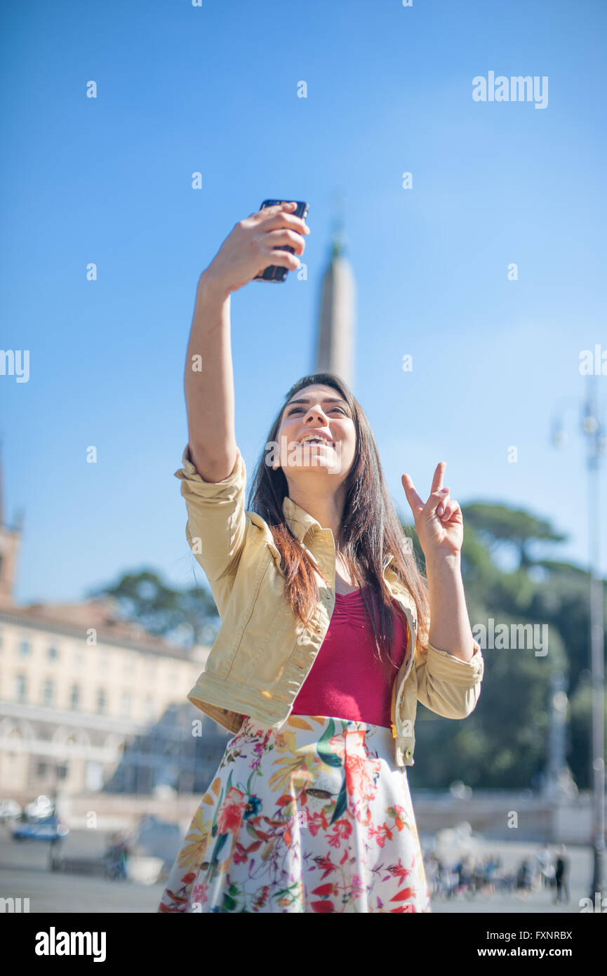 Giovane donna turistica prendendo selfie foto con il telefono cellulare a Roma il luogo con il segno della vittoria Foto Stock