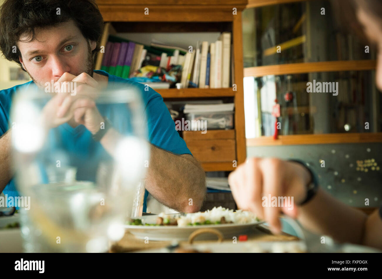 Uomo seduto al tavolo per la cena con le mani incrociate davanti alla bocca Foto Stock