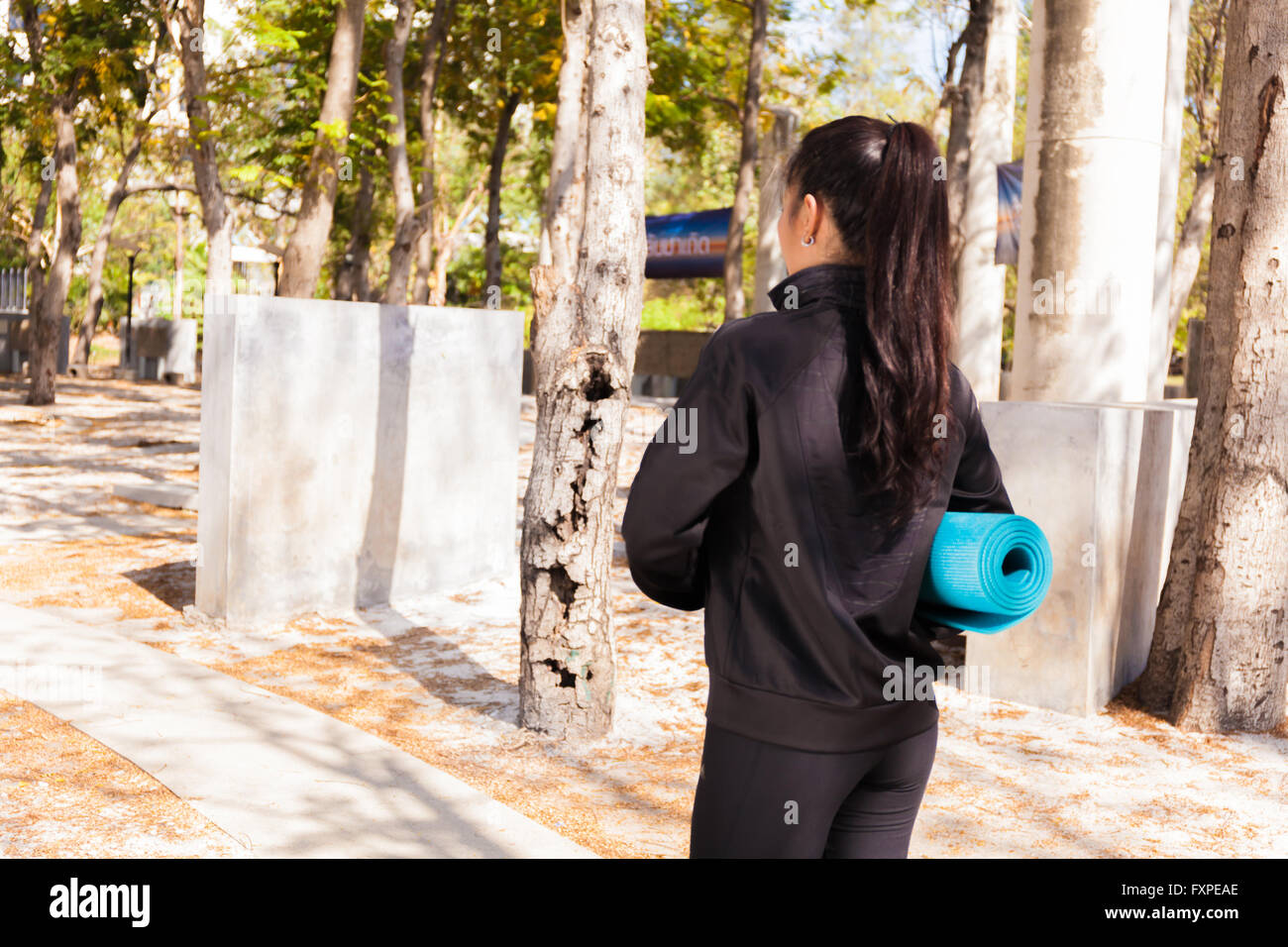 Giovani asiatici donna fitness tenendo un tappetino e andando a unirsi a lezione di yoga nel parco Foto Stock