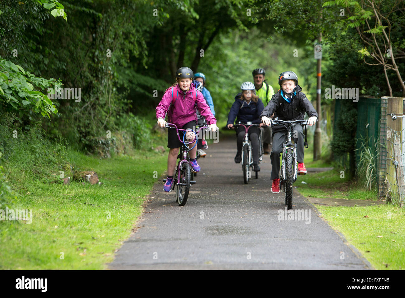 I bambini in modo sicuro il ciclismo a scuola con la supervisione di un adulto su pathways Foto Stock