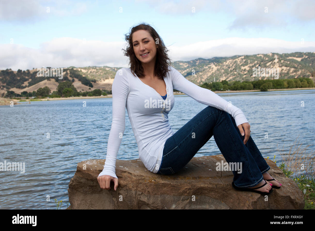 Giovane donna seduta su roccia lago nuvole di bordo Foto Stock