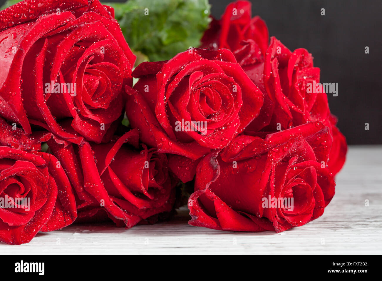 Bouquet di rose rosse con acqua gocce di rugiada sul bianco rustico in legno tavolo. Profondità di campo. Foto Stock