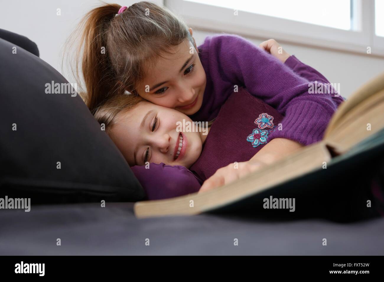 Superficie di visualizzazione del livello di una ragazza che sta sdraiato sul divano libro lettura, avvolgente e sorridente Foto Stock