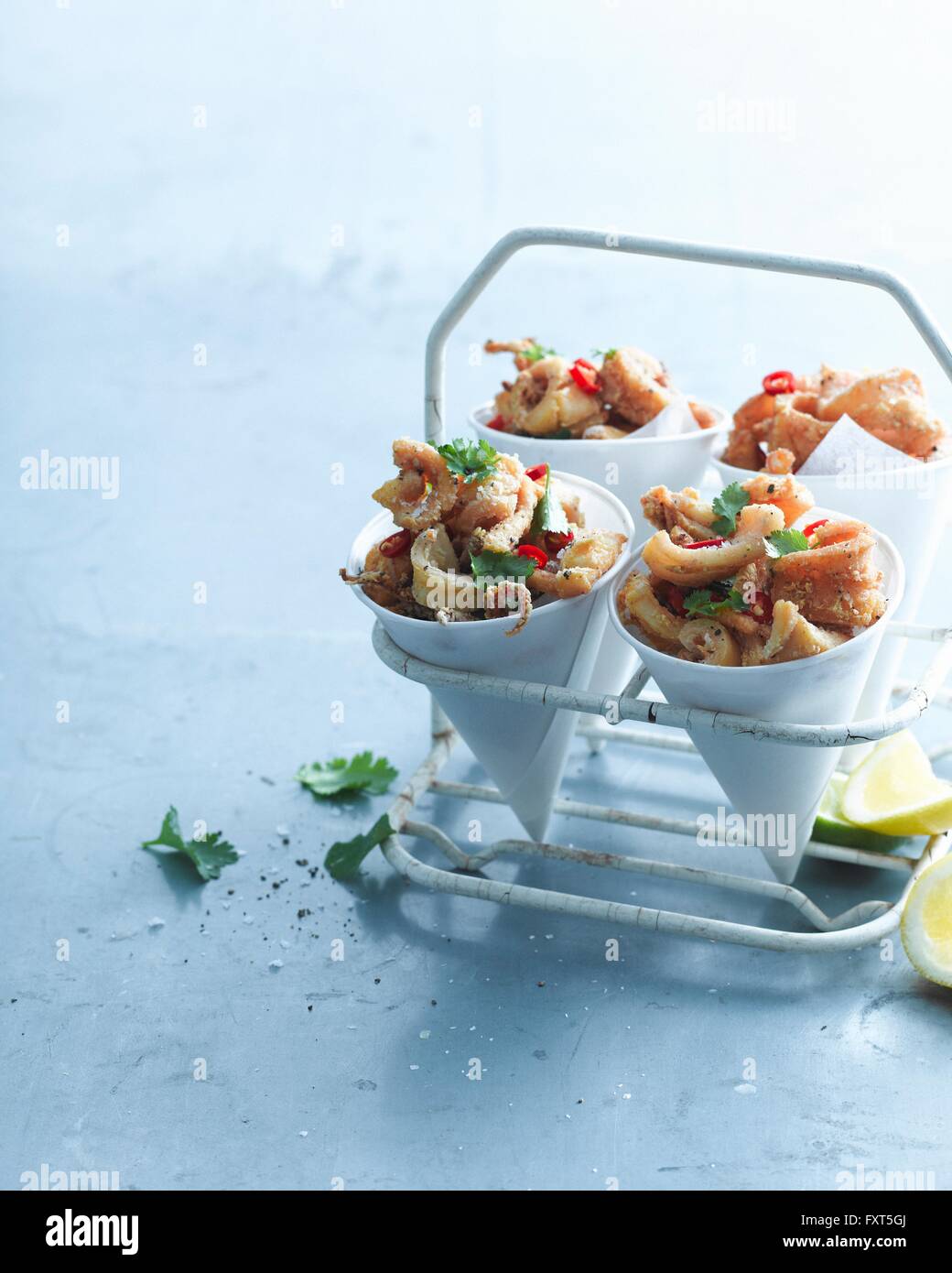 Sale e pepe peperoncino calamari guarnita con limone e coriandolo in coni di carta Foto Stock