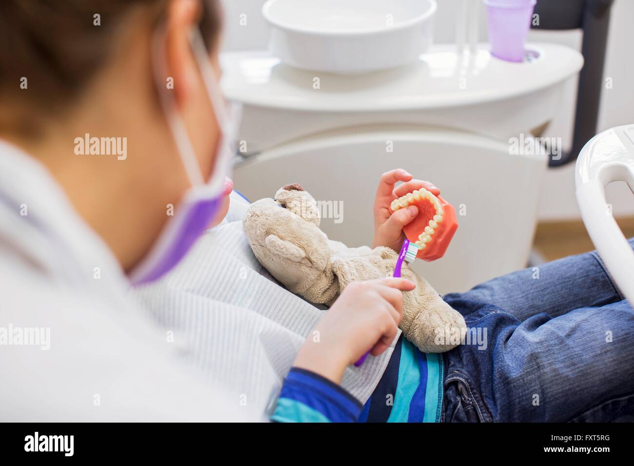 Vista ritagliata del ragazzo in poltrona del dentista holding orsacchiotto spazzolatura dentiere Foto Stock