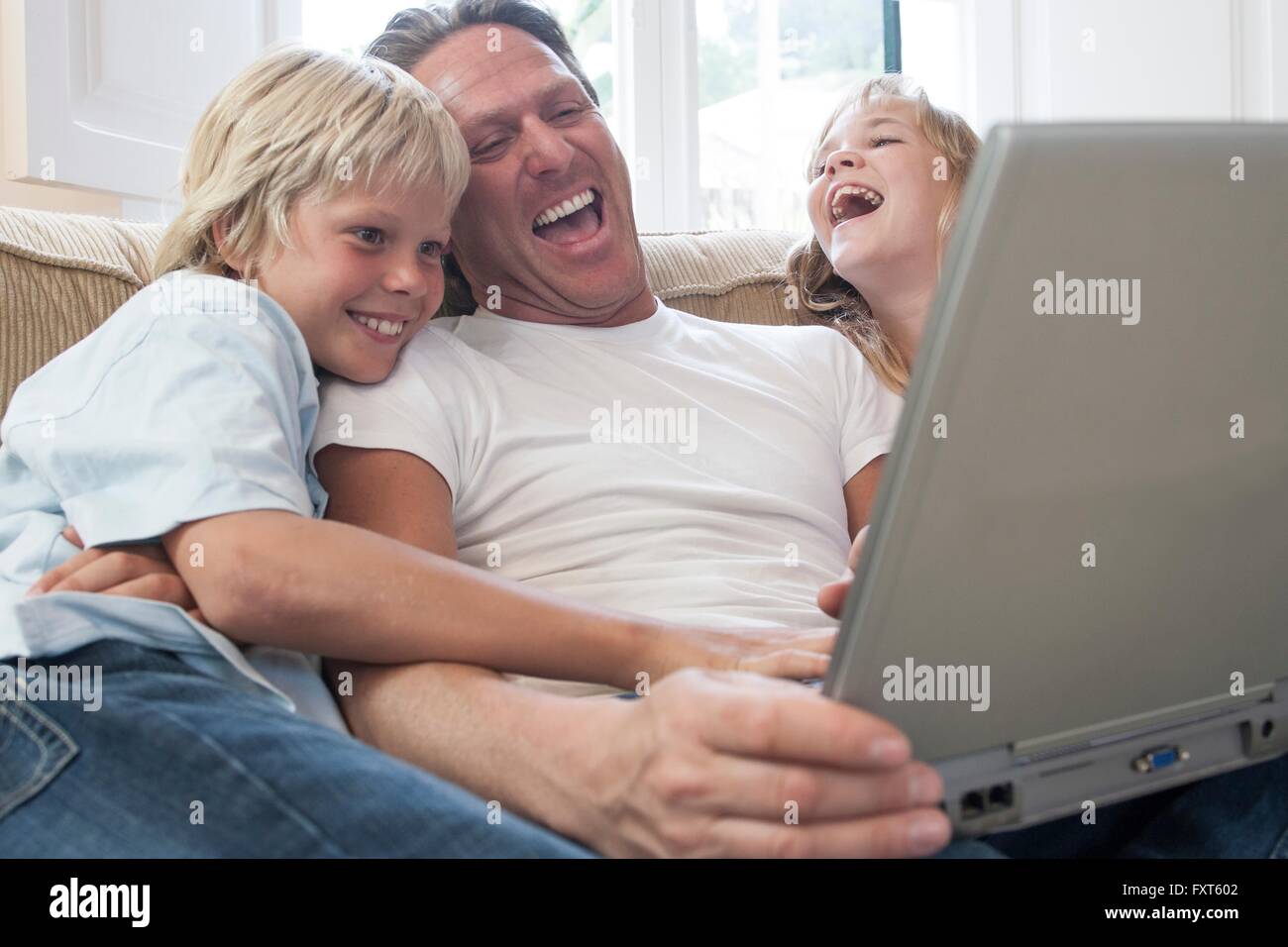 Padre e figli di ridere, utilizzando computer portatile in salotto Foto Stock