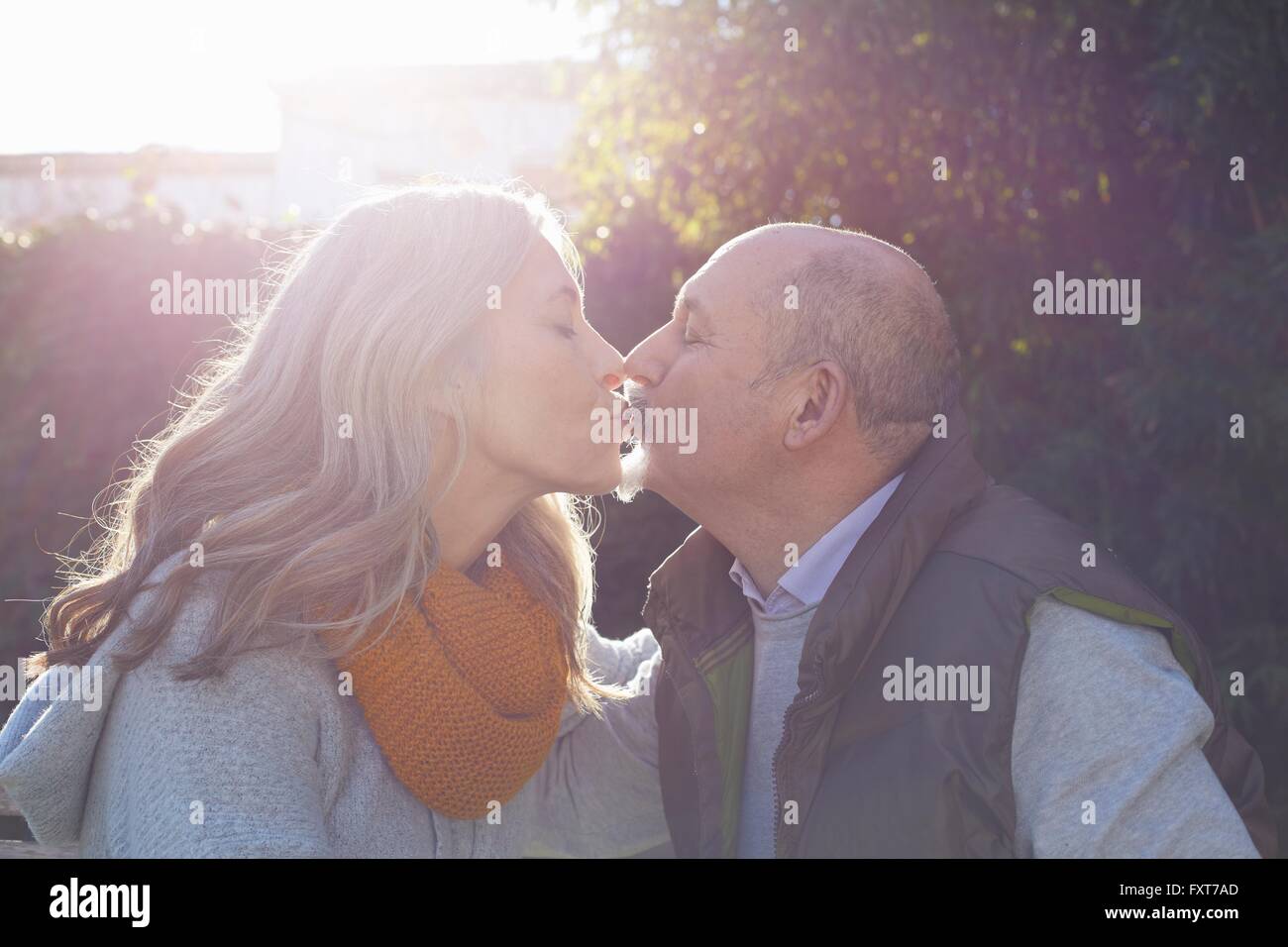 Coppia matura faccia a faccia baciare in presenza di luce solare Foto Stock