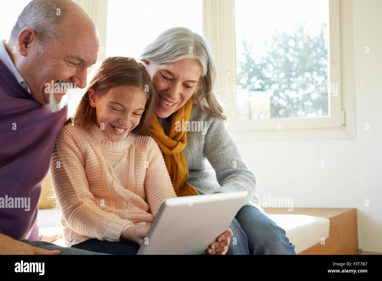 Nonni sulla finestra sedile utilizzando tavoletta digitale con il nipote guardando giù sorridente Foto Stock