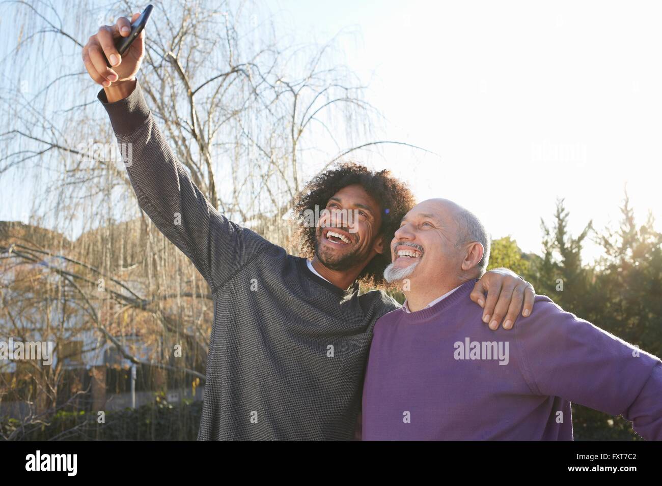 Gli uomini con le braccia intorno a ogni altro utilizza lo smartphone per prendere selfie sorridente Foto Stock