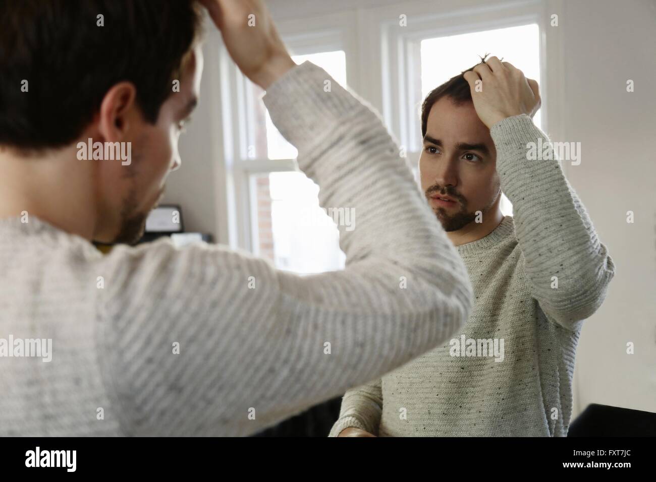 Metà uomo adulto guardando in uno specchio, controllare i capelli Foto Stock