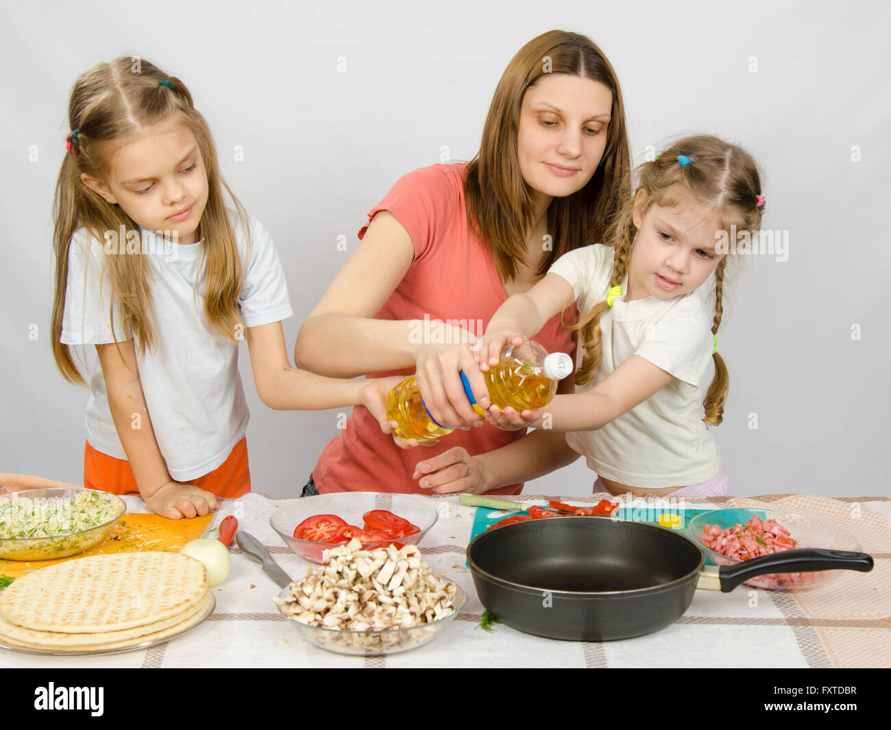 Due bambine al tavolo della cucina con entusiasmo per aiutare mia madre a versare olio vegetale in una padella Foto Stock