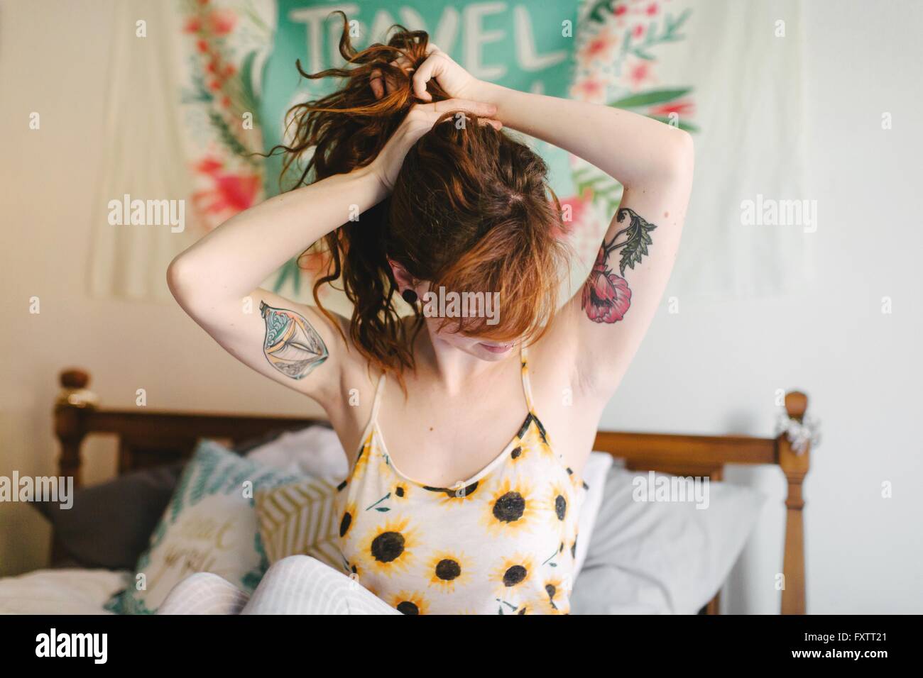 Giovane donna seduta sul letto, mettendo i capelli fino a coda di cavallo Foto Stock