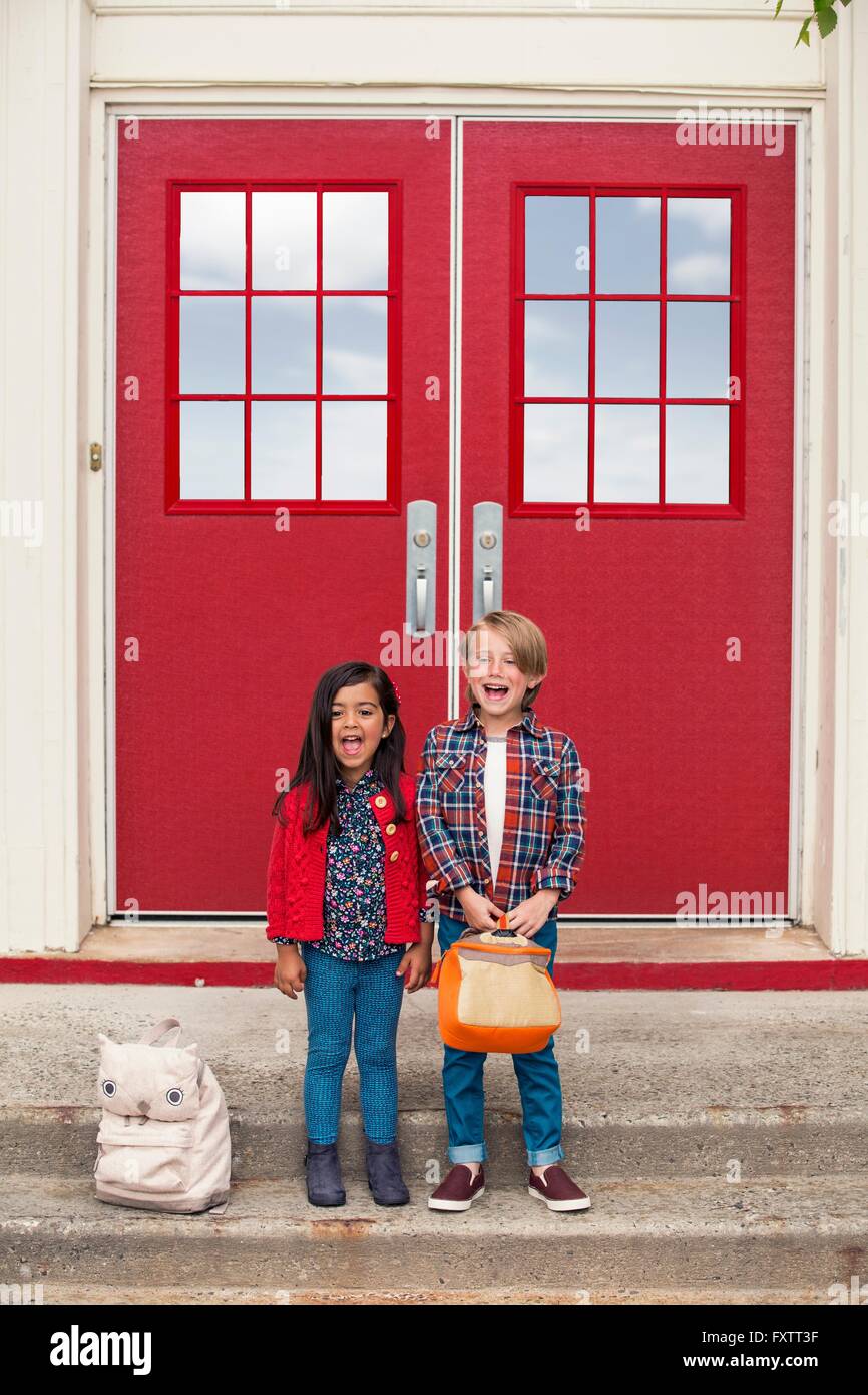 Ritratto di elementare schoolgirl e ragazzo con cartelle di scuola alle elementari porta Foto Stock