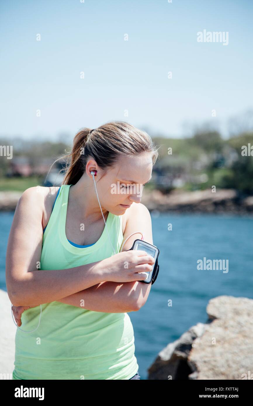 Donna che indossa gli auricolari guardando il tracker di attività su braccio Foto Stock